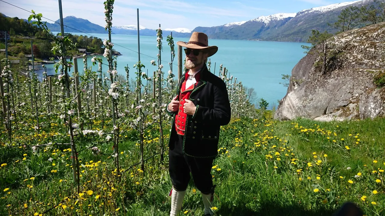 Knut André i hardangerbunad i ein blomstrande frukthage over Hardangerfjorden.